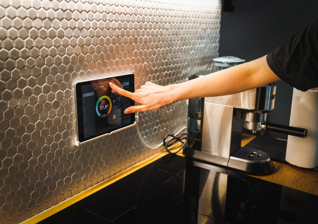 pexels-photo-16423103 Modern kitchen scene featuring a hand using a tablet to control a smart home system.